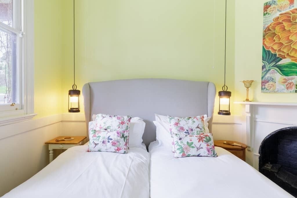 Una cama doble con almohadas florales, dos mesitas de noche, una chimenea y una ventana con vistas.