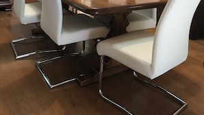 Un comedor con una mesa de madera y sillas blancas con patas cromadas.