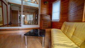 Interior de una cabaña de madera con sofá, mesa y puerta corrediza de vidrio que da a un balcón.