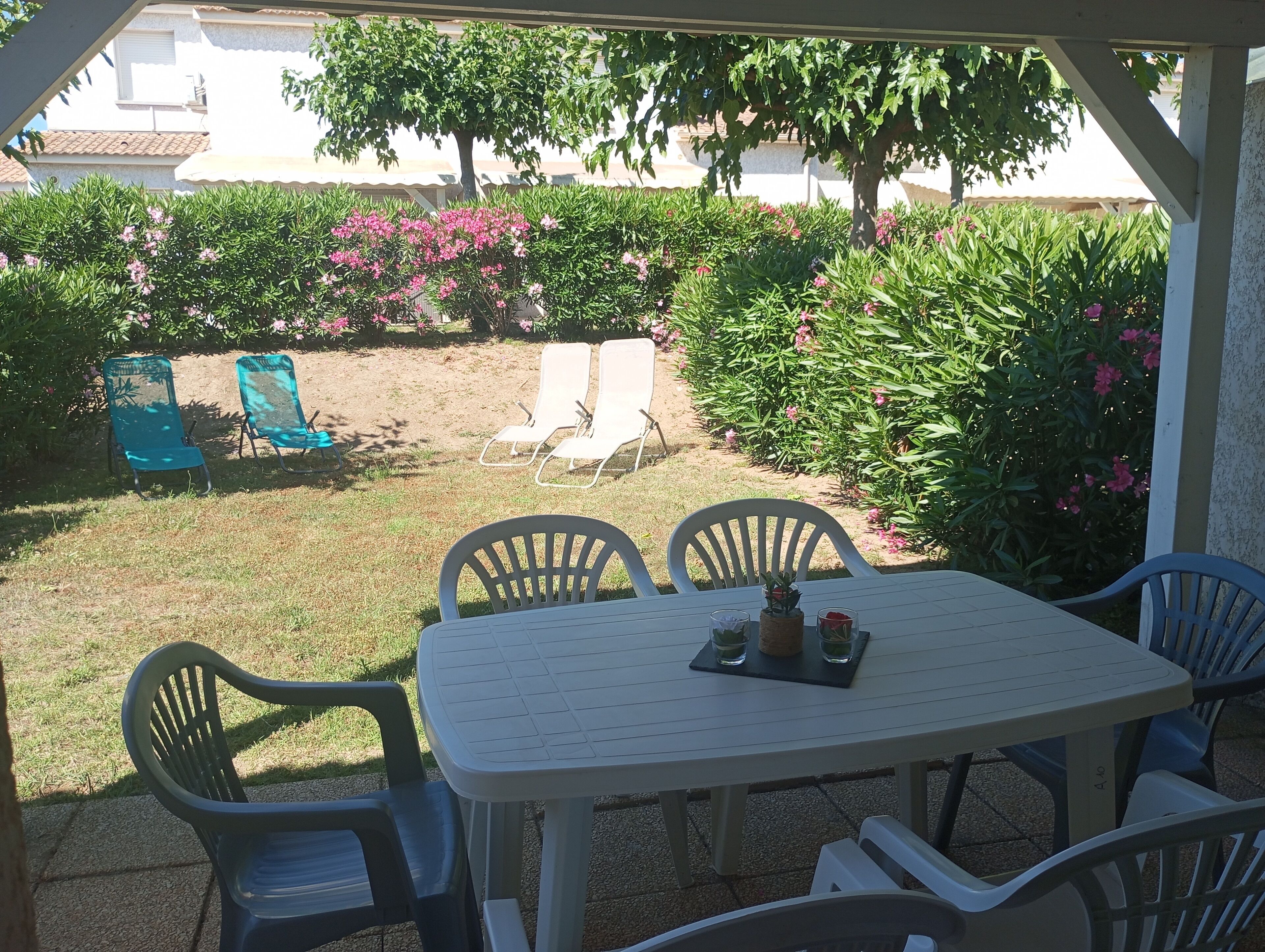 Une terrasse extérieure avec une table et des chaises, entourée d’une végétation luxuriante et de plantes en fleurs.
