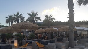 A beachside lounge with wicker furniture, thatched umbrellas, and palm trees.