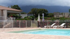 A swimming pool with lounge chairs, a fenced area, and a building with a tiled roof.