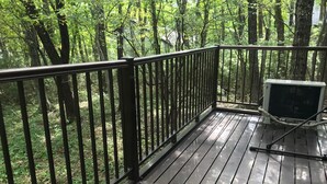 Una terraza de madera con barandas de metal, rodeada de densa vegetación verde.