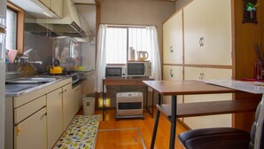 Una cocina compacta con microondas, hervidor y lavabo. Hay una pequeña mesa y una silla.