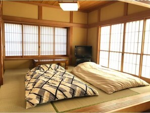 A traditional Japanese room with tatami flooring, a bed with patterned bedding, and a television on a low stand. - BBQ House (Nasu)