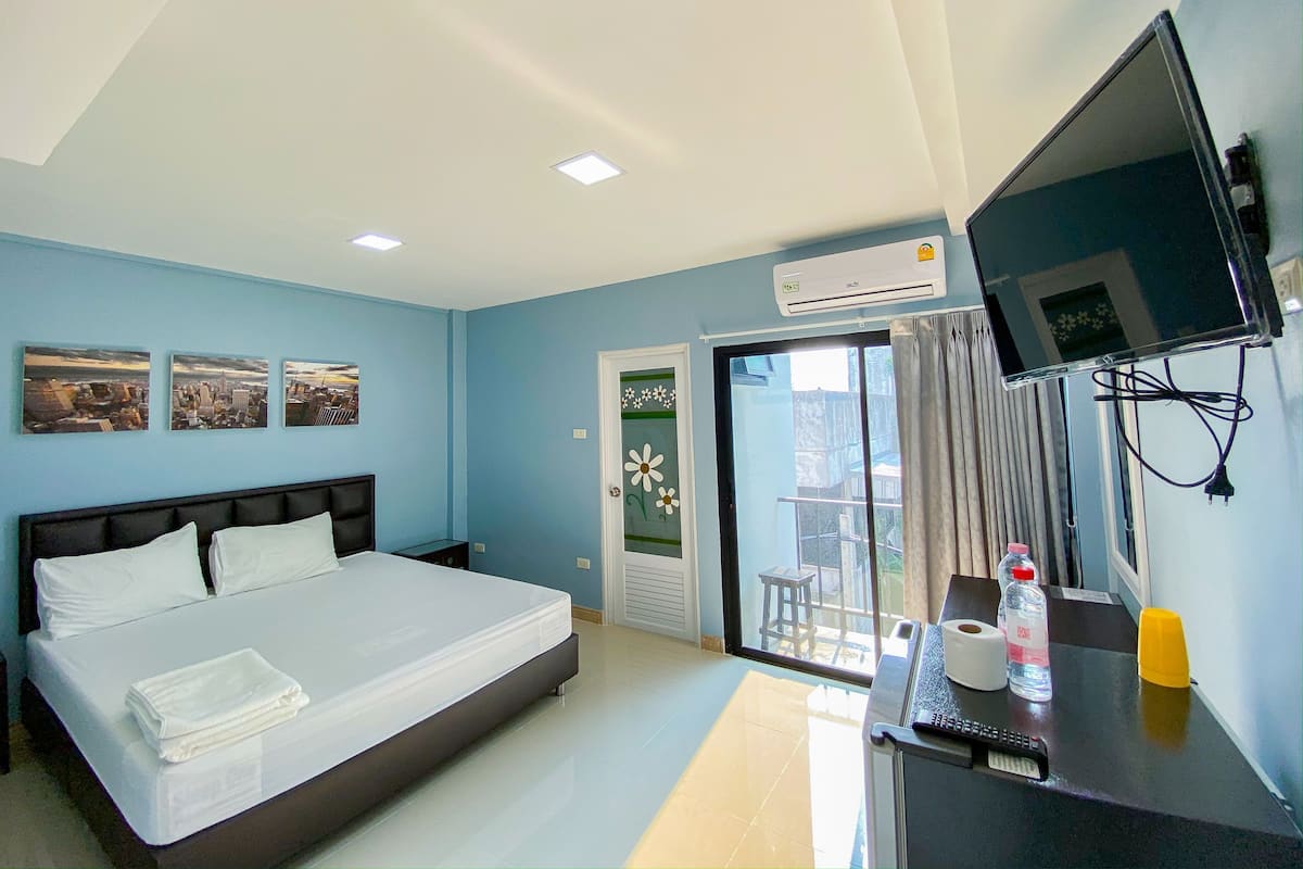 A hotel room with a bed, a desk with a TV, and a sliding glass door to the outside.