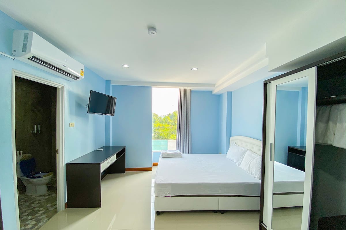 A bedroom with a bed, a TV, a desk, and an air conditioning unit.