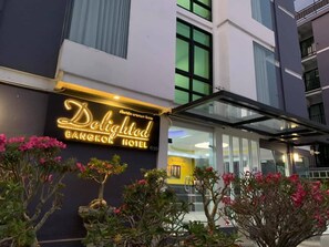 The exterior of the Delighted Bangkok Hotel with a prominent illuminated sign, a glass entrance, and surrounding greenery. - Delighted Bangkok Hotel (Bangkok)