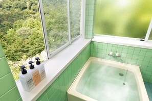 A bathroom with a bathtub, green tiles, and bottles of shampoo and conditioner on the windowsill. - A villa in the forest in Minamikaruizawa (Shimonita)