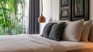 Een bed met een beige sprei, twee kussens en een hanglamp.