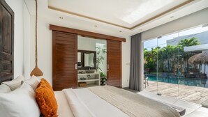 Een moderne slaapkamer met een groot bed, een houten deur, een glazen deur naar een zwembadgedeelte en uitzicht op de omgeving.