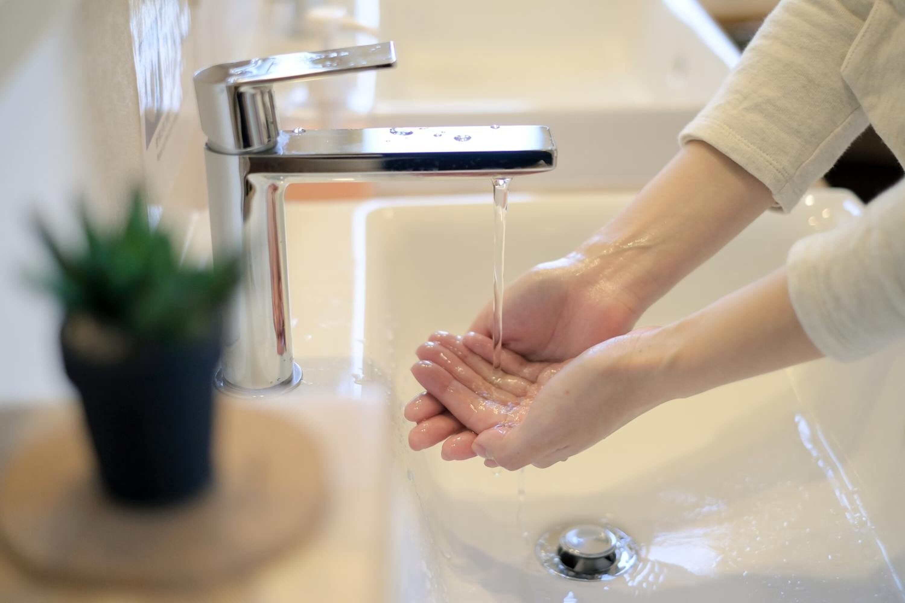 Una mano sotto un rubinetto aperto in un lavabo da bagno.
