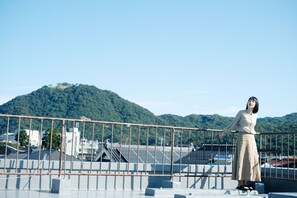 Una persona de pie en la azotea, con vistas a una montaña y edificios al fondo.