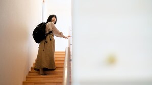 Una persona baja por una escalera de madera en un edificio de paredes blancas.