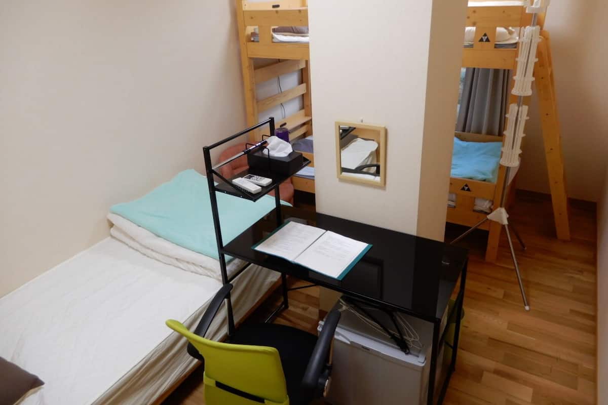 A compact room with a bunk bed, a desk with a chair, a small table, and a mirror.