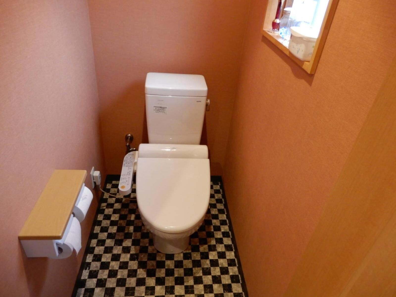 Un baño pequeño con inodoro, dispensador de papel higiénico y piso de cuadros.