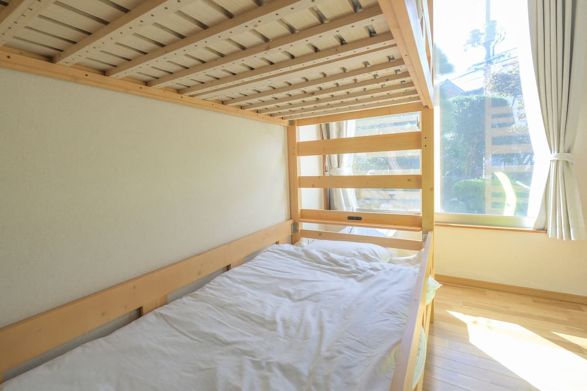 A single bed with a wooden frame and white bedding in a room with a sloped ceiling and a window with curtains.