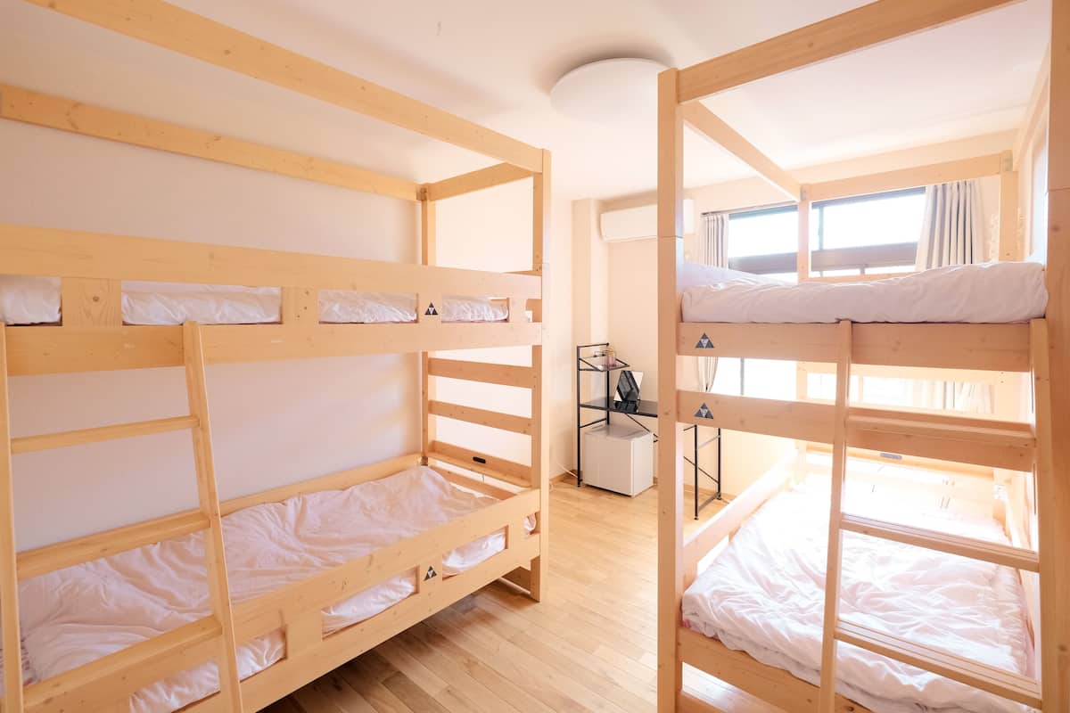 A dormitory room with bunk beds, a small desk, and a window.