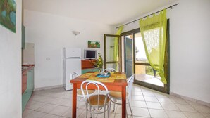 A compact kitchen with a refrigerator, a dining table with chairs, and a television.
