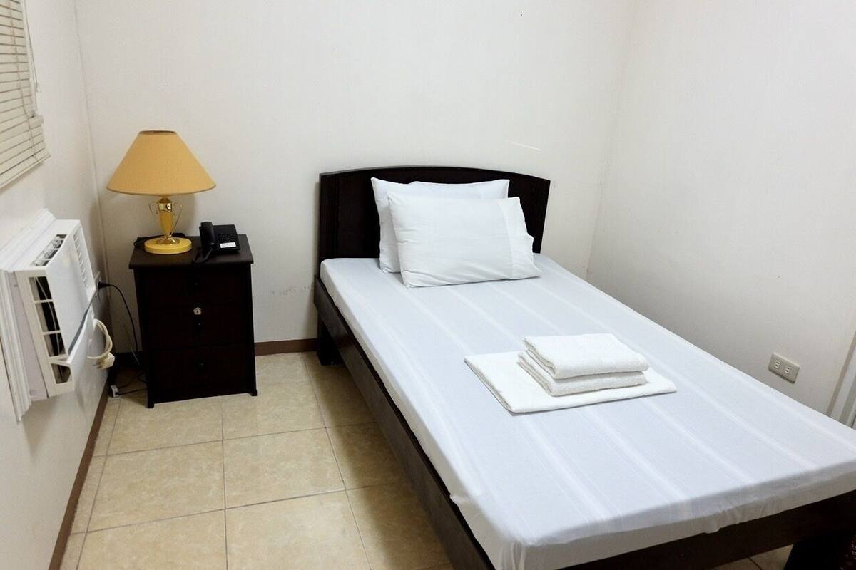 A single bed with white bedding, a bedside lamp, and a black nightstand with a phone.