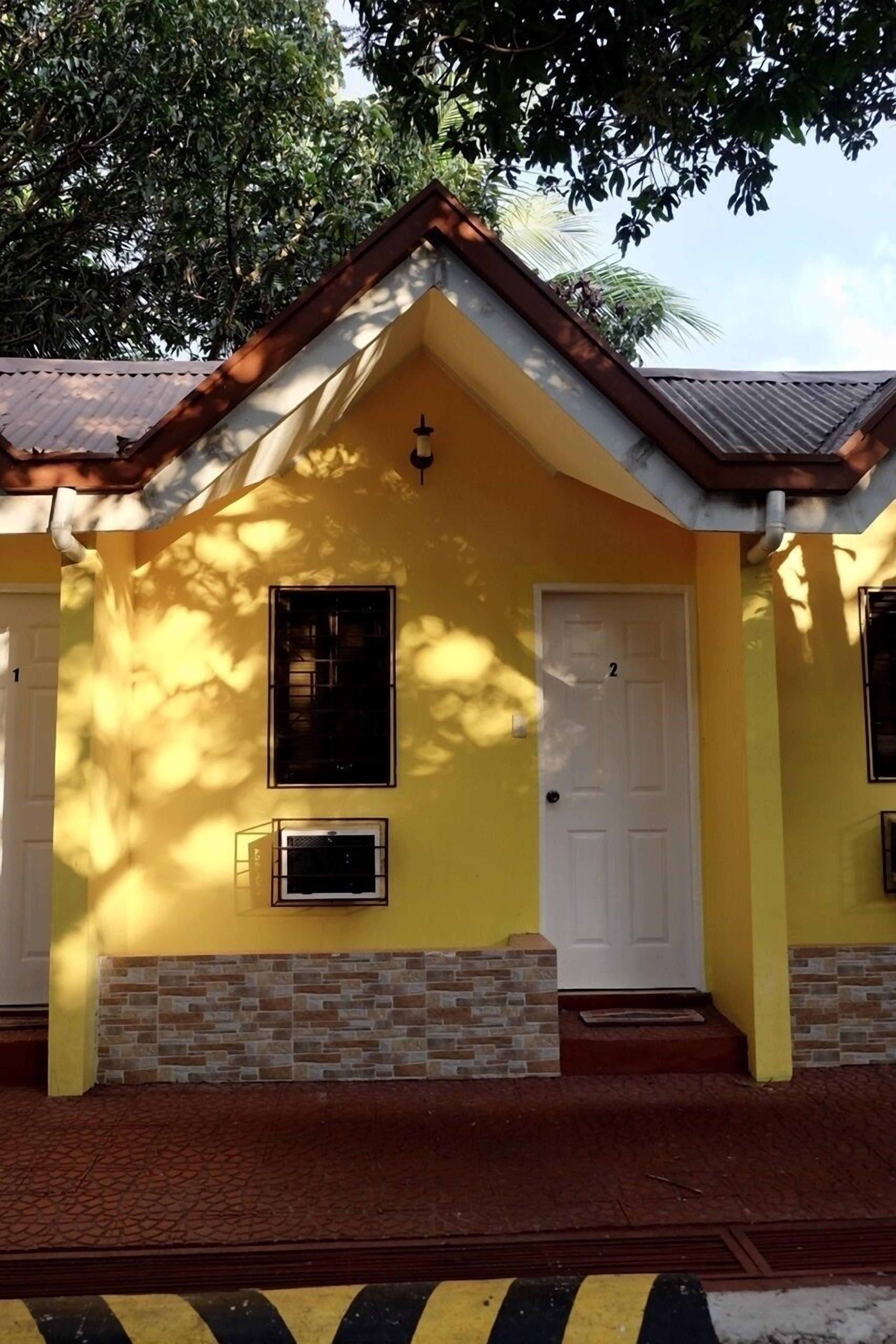Un bâtiment jaune avec deux portes, une fenêtre et un socle en briques.