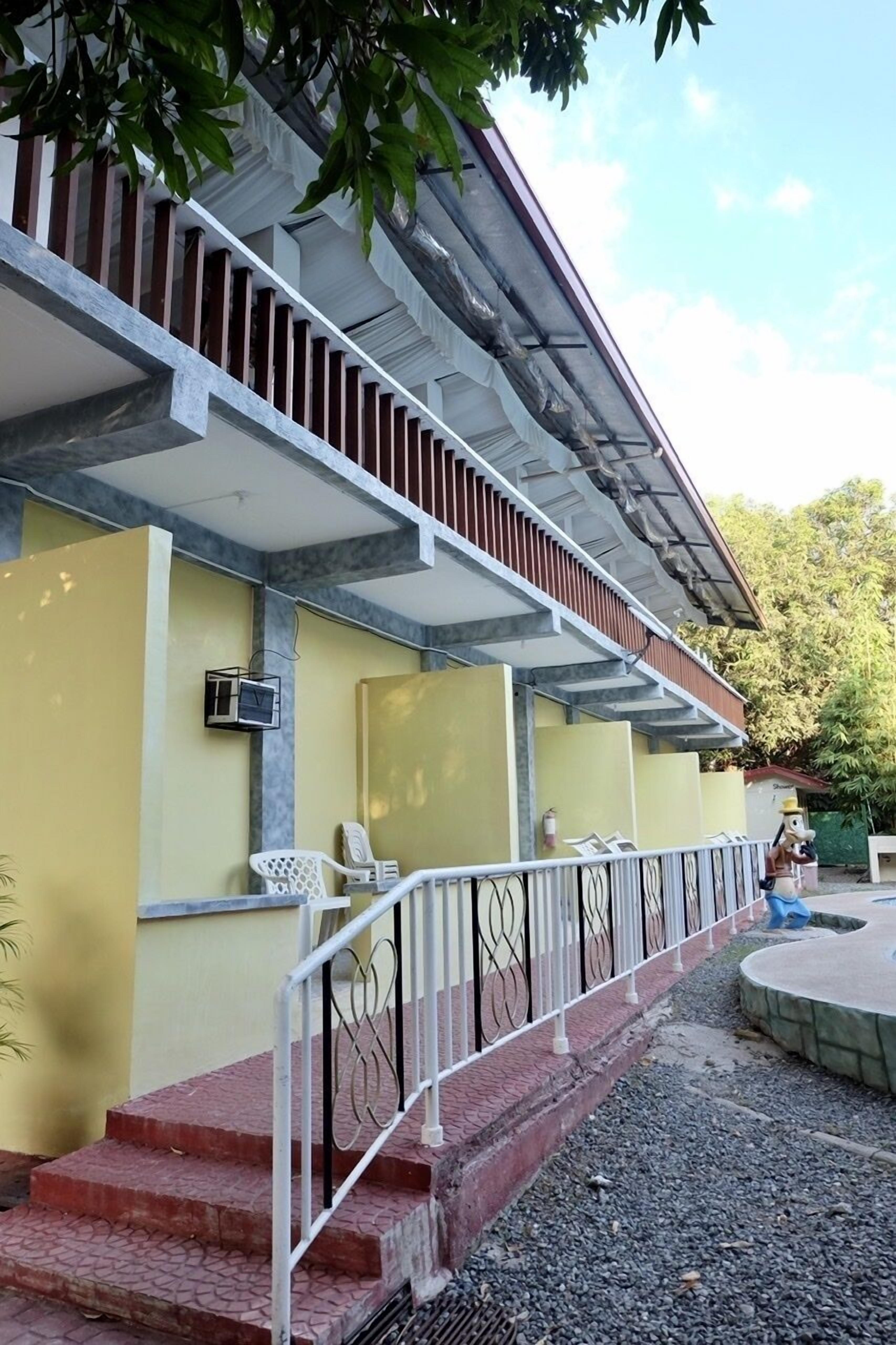 Un edificio con fachada amarilla, un porche cubierto con escalones y una barandilla de metal.