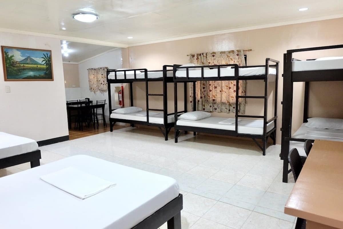 A dormitory room with bunk beds, a dining table, and a painting on the wall.