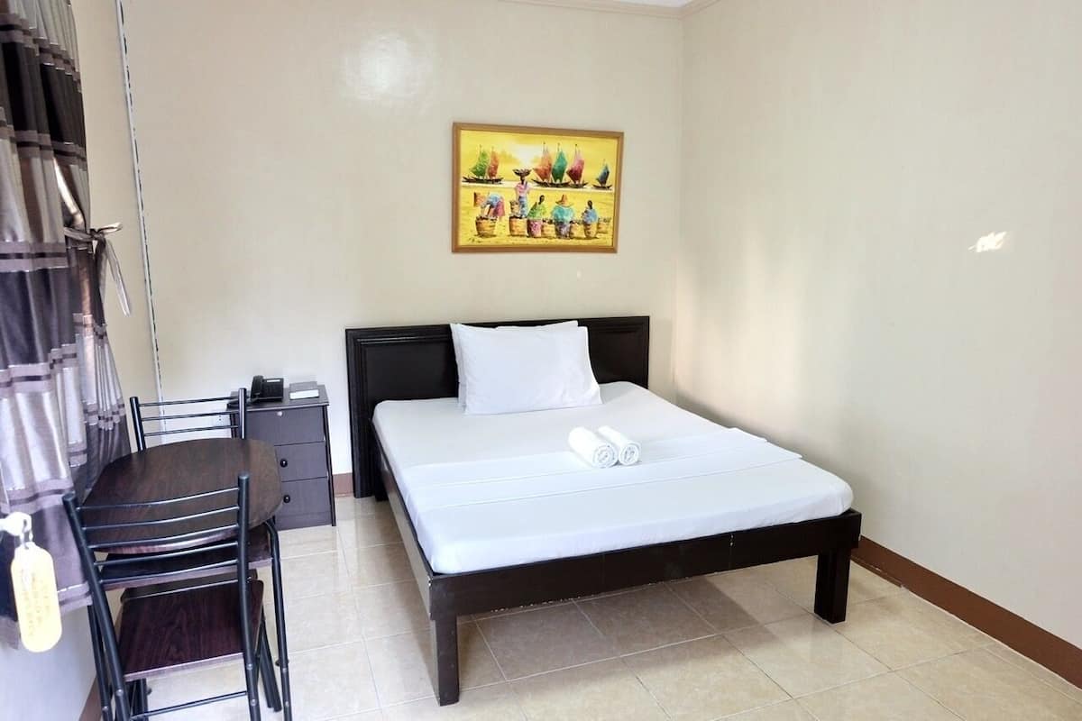 A hotel room with a bed, a desk, a chair, a nightstand, and a painting on the wall.