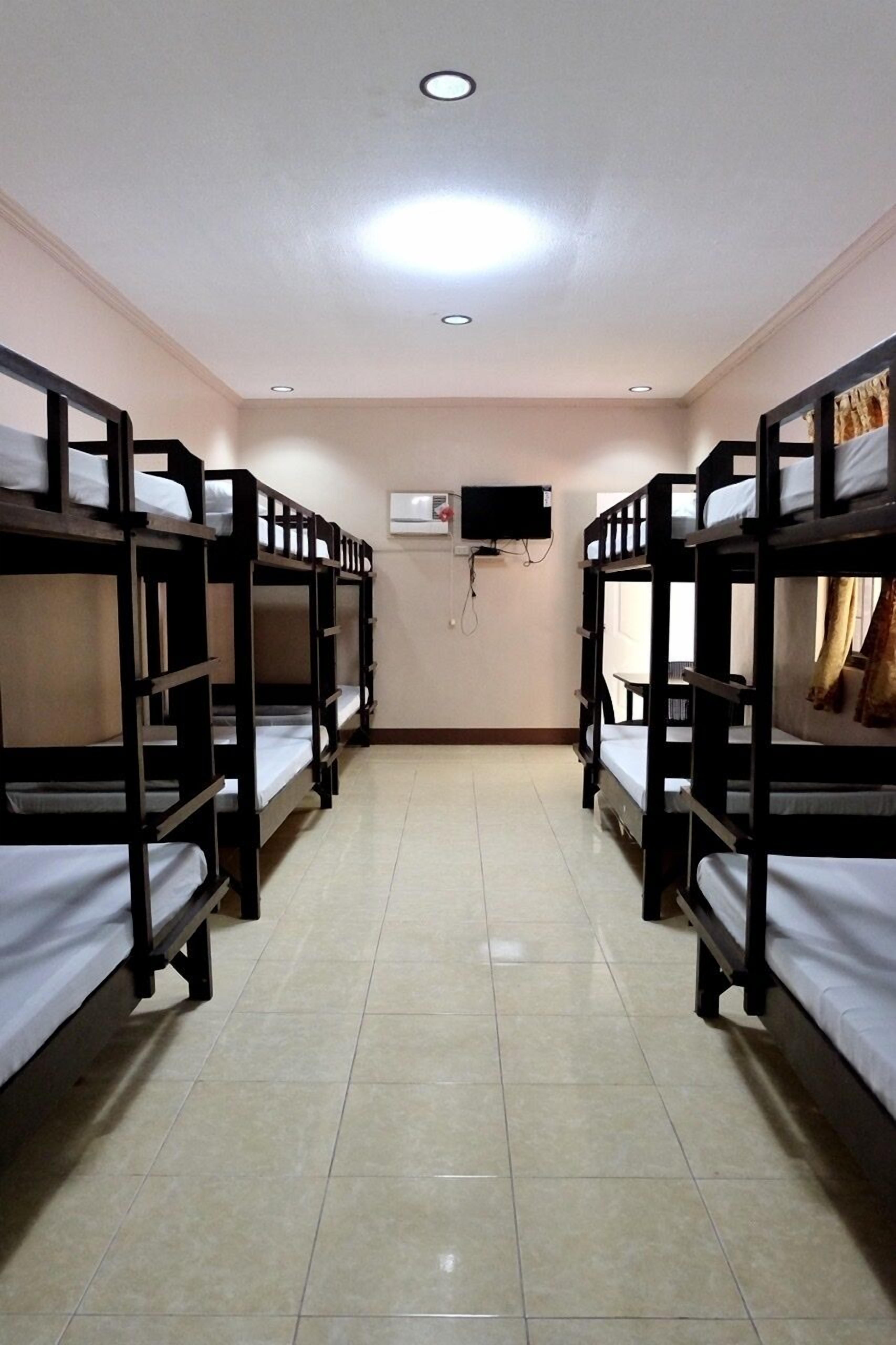 A room with bunk beds arranged in two rows, a flat-screen TV mounted on the wall, and a ceiling light.