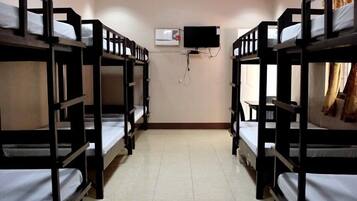A room with bunk beds arranged in two rows, a flat-screen TV mounted on the wall, and a ceiling light.