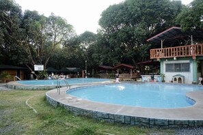 Relax by the serene pool surrounded by lush greenery and enjoy dining and seating areas under shaded umbrellas.