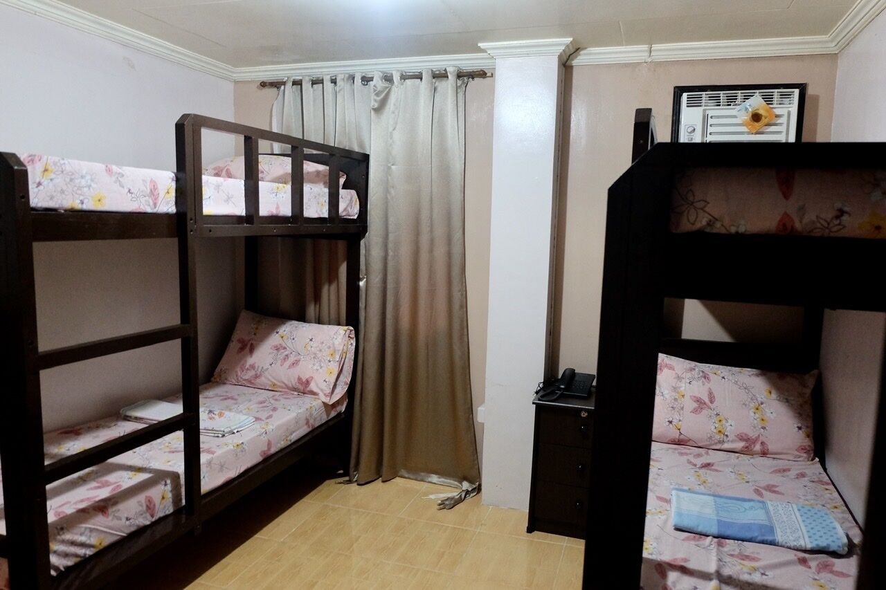A room with two bunk beds, a small desk, a chair, and a curtain.