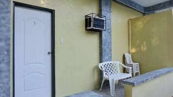 A room with a white door, a small air conditioning unit mounted on the wall, and two white plastic chairs against a yellow wall.