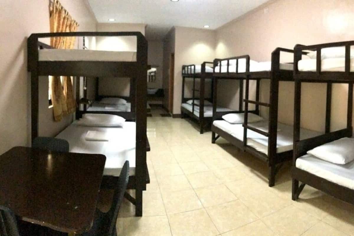 A dormitory room with bunk beds, a table, and chairs.