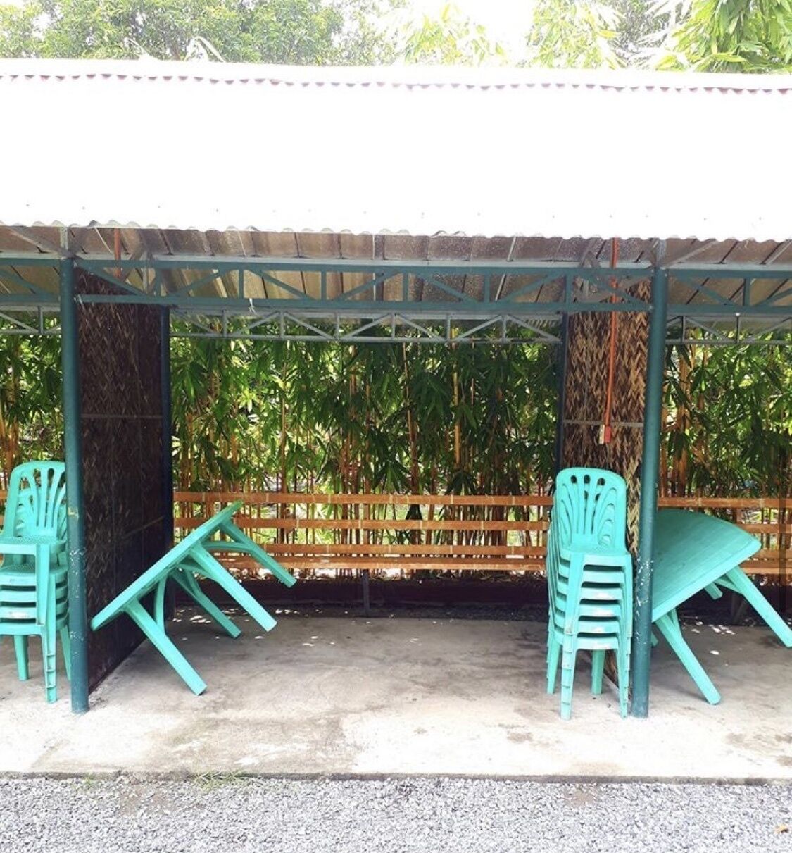 A covered outdoor seating area with two green plastic chairs and a bench.