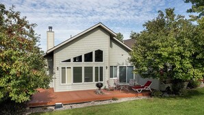 Una casa con techo inclinado, ventanas amplias y un patio con mobiliario exterior.