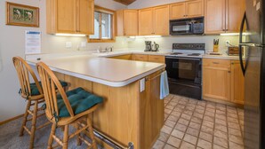 Una cocina con armarios de madera, una isla central con taburetes de bar, microondas, estufa y refrigerador.