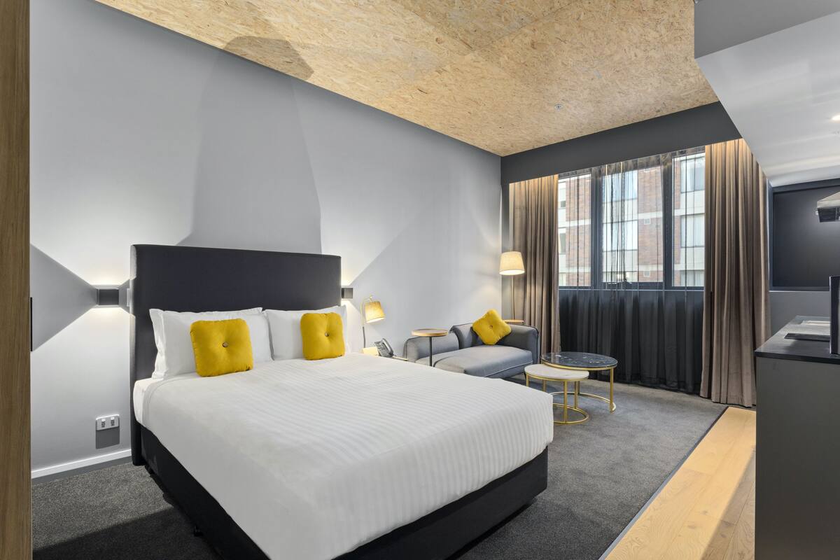 A modern hotel room with a large bed, a sofa, a small table, and a TV.