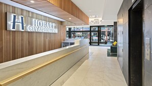 Una recepción con un cartel de Hobart City Apartments, un interior moderno con paneles de madera y un ascensor.