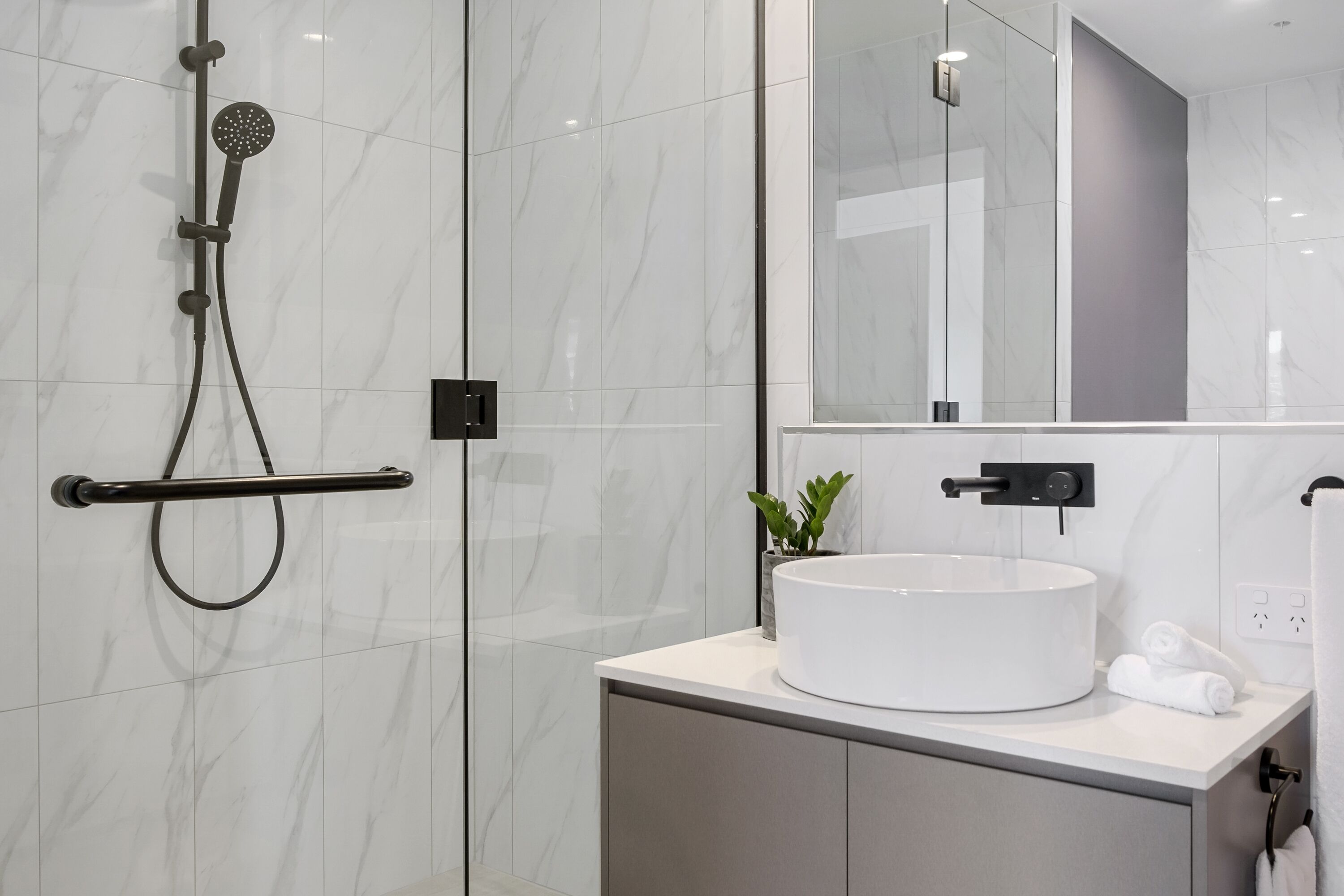 Une salle de bain moderne avec une douche à parois de verre, un lavabo blanc et un miroir au-dessus du lavabo.