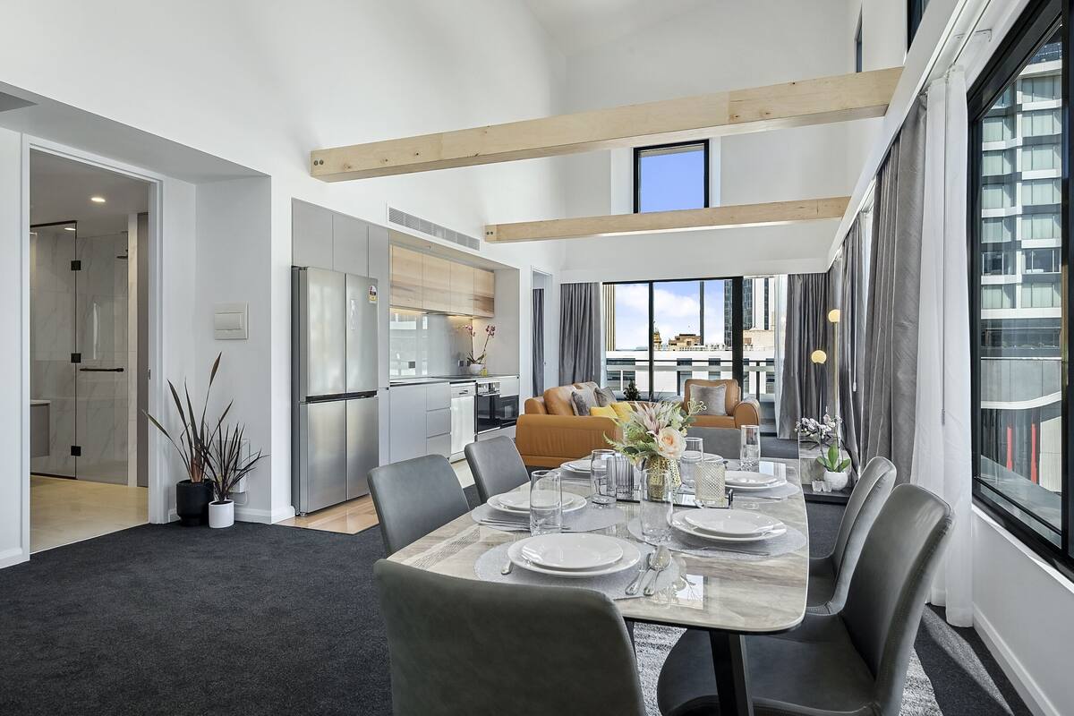 A modern dining area with a marble table, grey chairs, and a view of the cityscape through large windows.