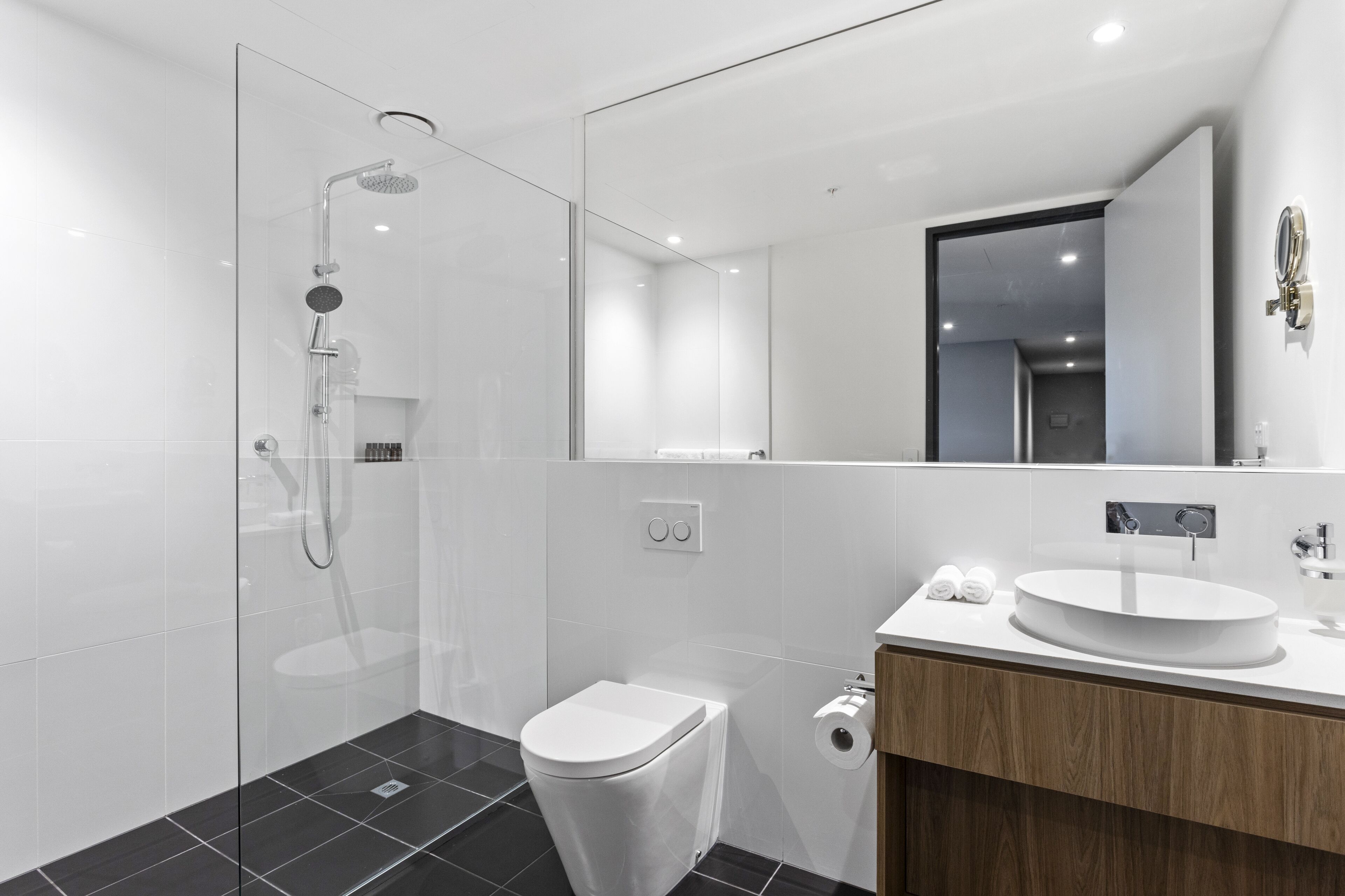 A modern bathroom with a glass shower enclosure, a white toilet, and a wooden vanity with a round sink.