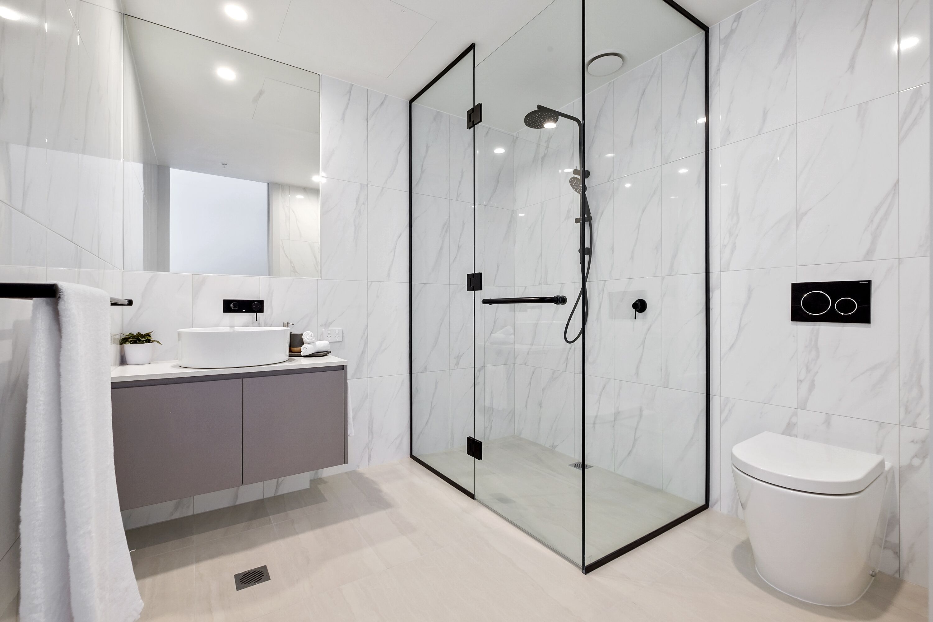 A modern bathroom with a glass-enclosed shower, a white toilet, and a vanity with a sink and mirror.