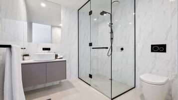 Et moderne badeværelse med et glasafskærmet brusebad, et hvidt toilet og et badeværelsesmøbel med vask og spejl.
