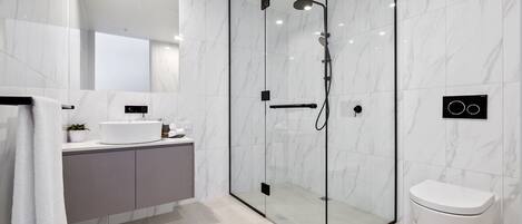 A modern bathroom with a glass-enclosed shower, a white toilet, and a vanity with a sink and mirror.
