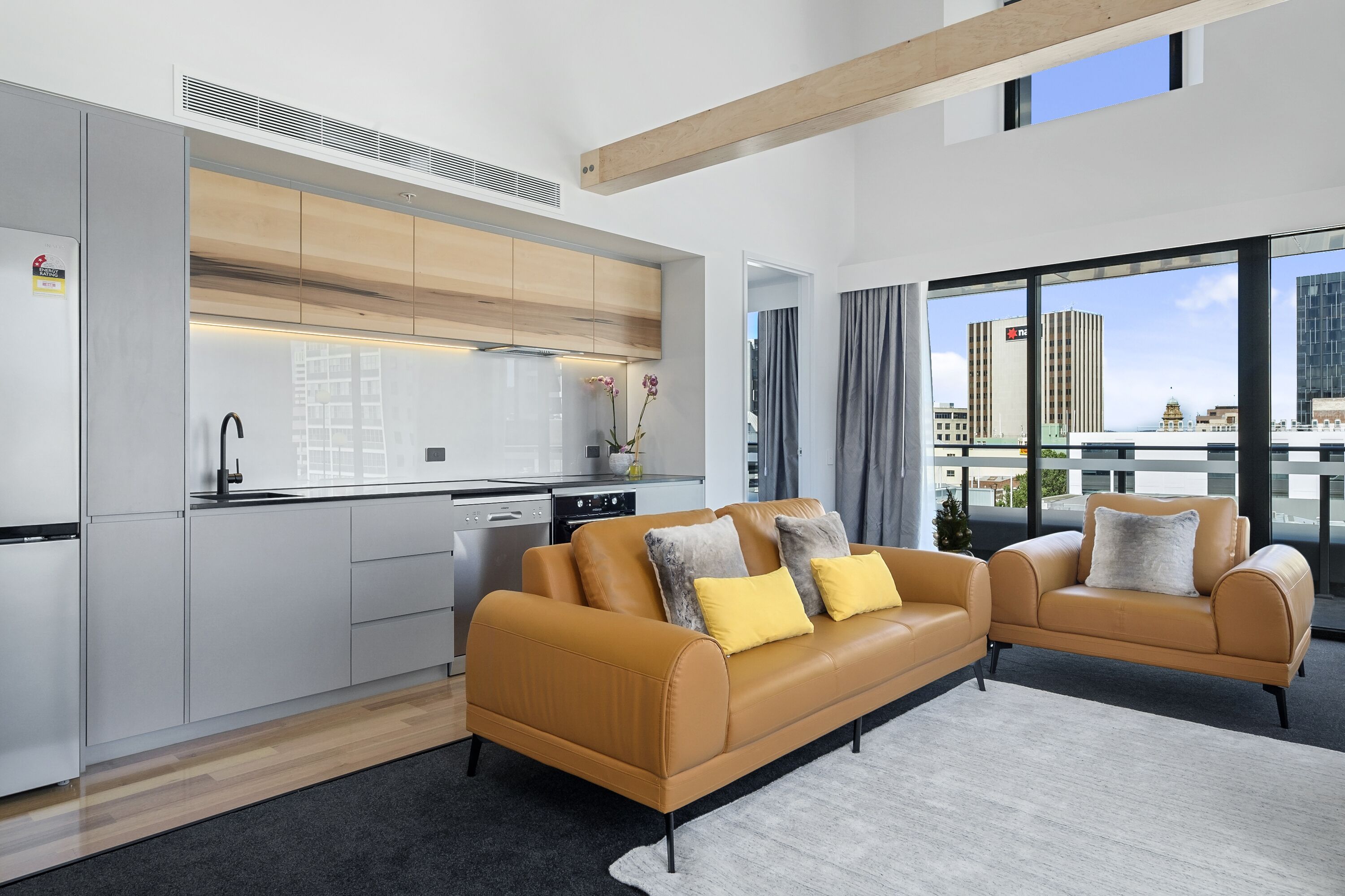 Un apartamento moderno con cocina, dos sofás y un amplio ventanal con vistas a la ciudad.