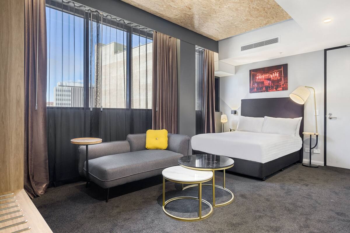 A hotel room with a bed, a sofa, a small round table, and a large window with curtains.