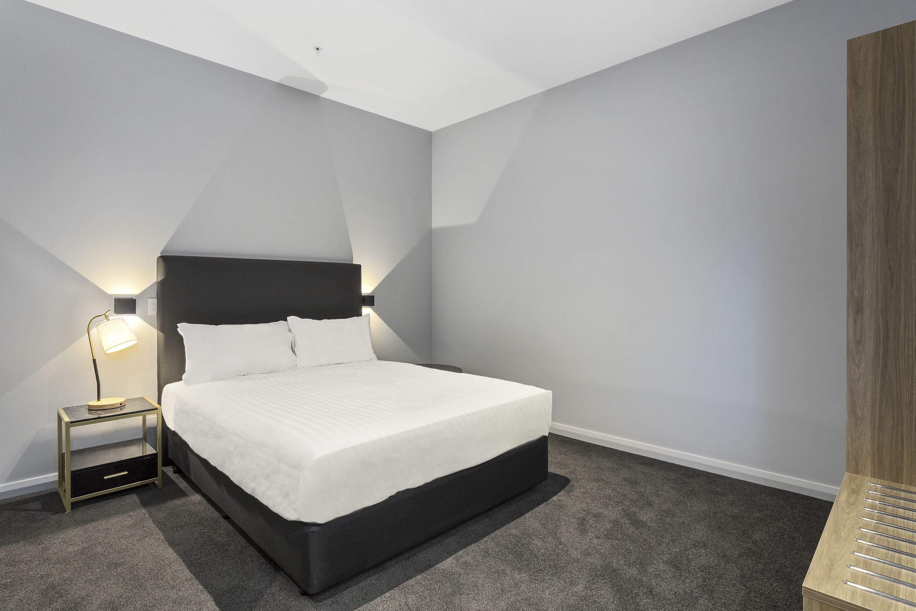 A modern bedroom with a bed, bedside table, lamp, and a wardrobe.