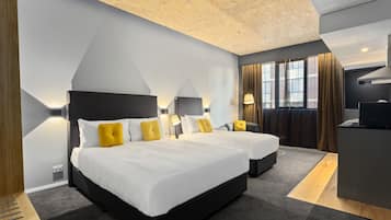 Habitación de hotel moderna con dos camas, un escritorio y un amplio ventanal con cortinas.