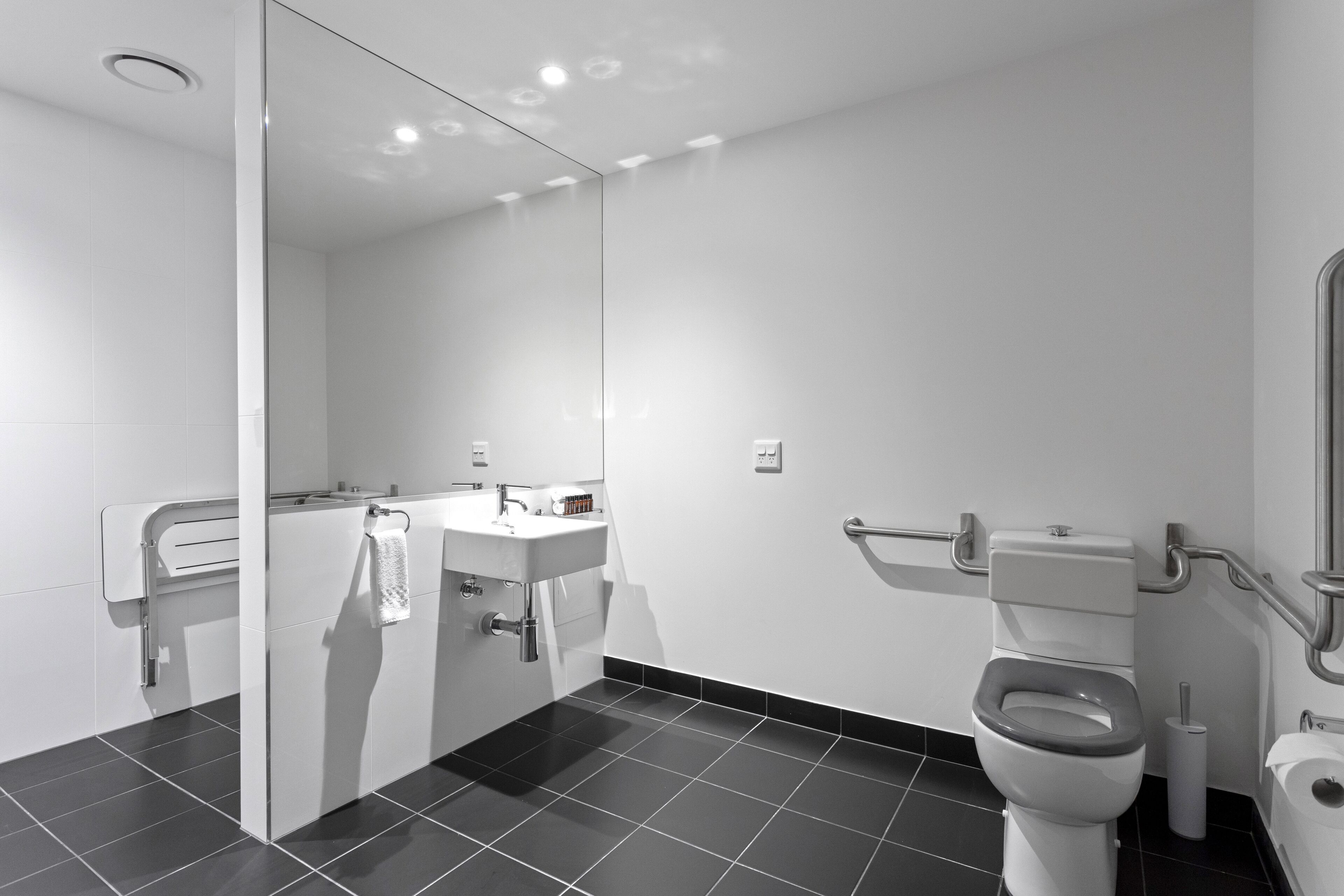 Une salle de bain moderne avec un lavabo, un miroir et des toilettes blancs, agrémentée d’un sol carrelé noir et d’une cloison en verre.